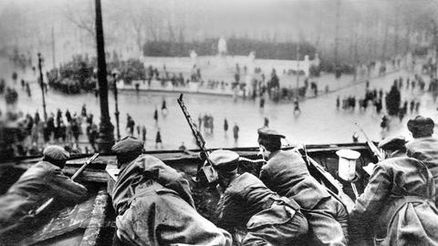 Auf dem Brandenburger Tor liegen Soldaten in Schießposition. Auf dem Platz darunter sieht man in der Menschen.