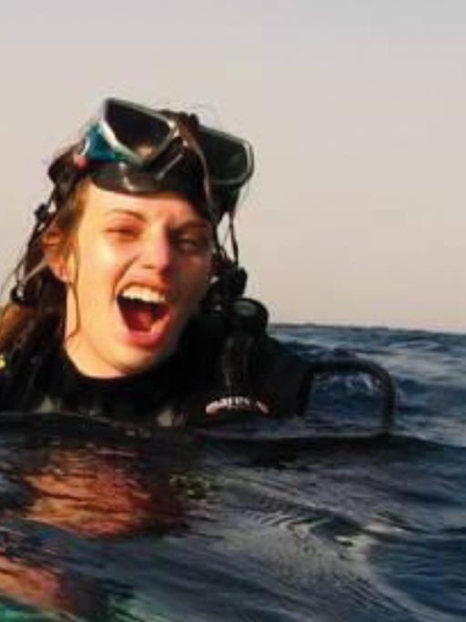 Julia Schnetzer schwimmt mit Tauschausrüstung im Meer und schaut fröhlich in die Kamera.