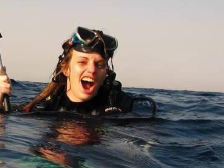 Julia Schnetzer schwimmt mit Tauschausrüstung im Meer und schaut fröhlich in die Kamera.