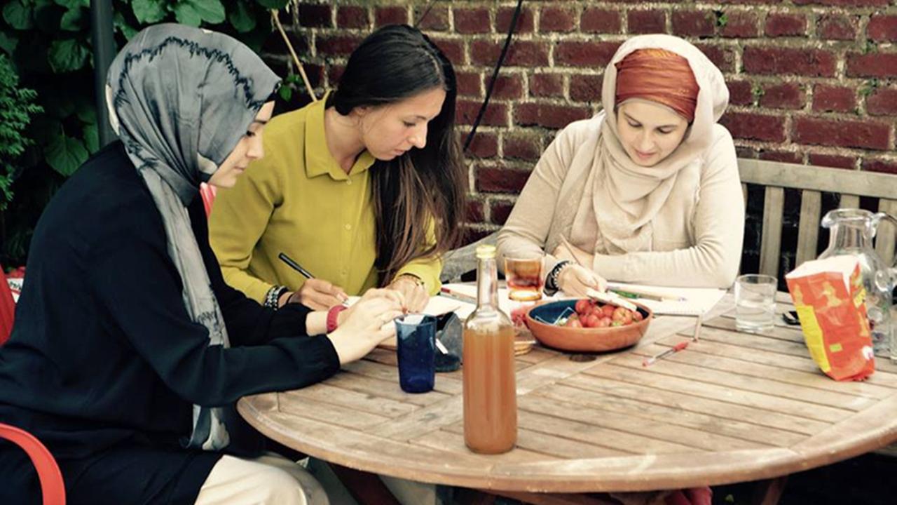 Zwei Frauen mit Kopftuch und eine weitere junge Frau sitzen an einem Gartentisch und arbeiten. Zwei Frauen mit Kopftuch und eine weitere junge Frau sitzen an einem Gartentisch und arbeiten.