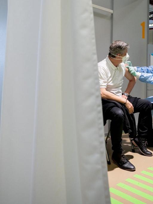 Einblick in eine Impfkabine, in der ein Arzt einem Mann gerade eine Spritze gibt