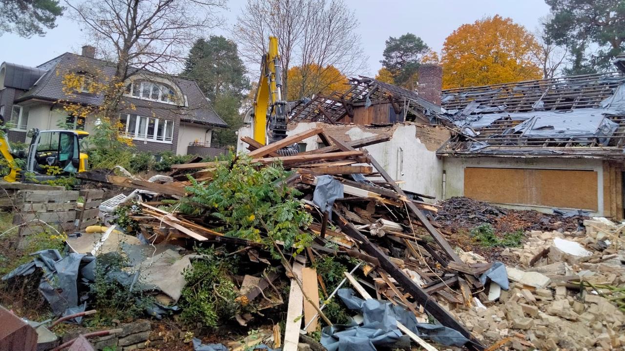 Ein Bagger steht hinter einem Schutthaufen vor einem halb abgerissenem Haus.