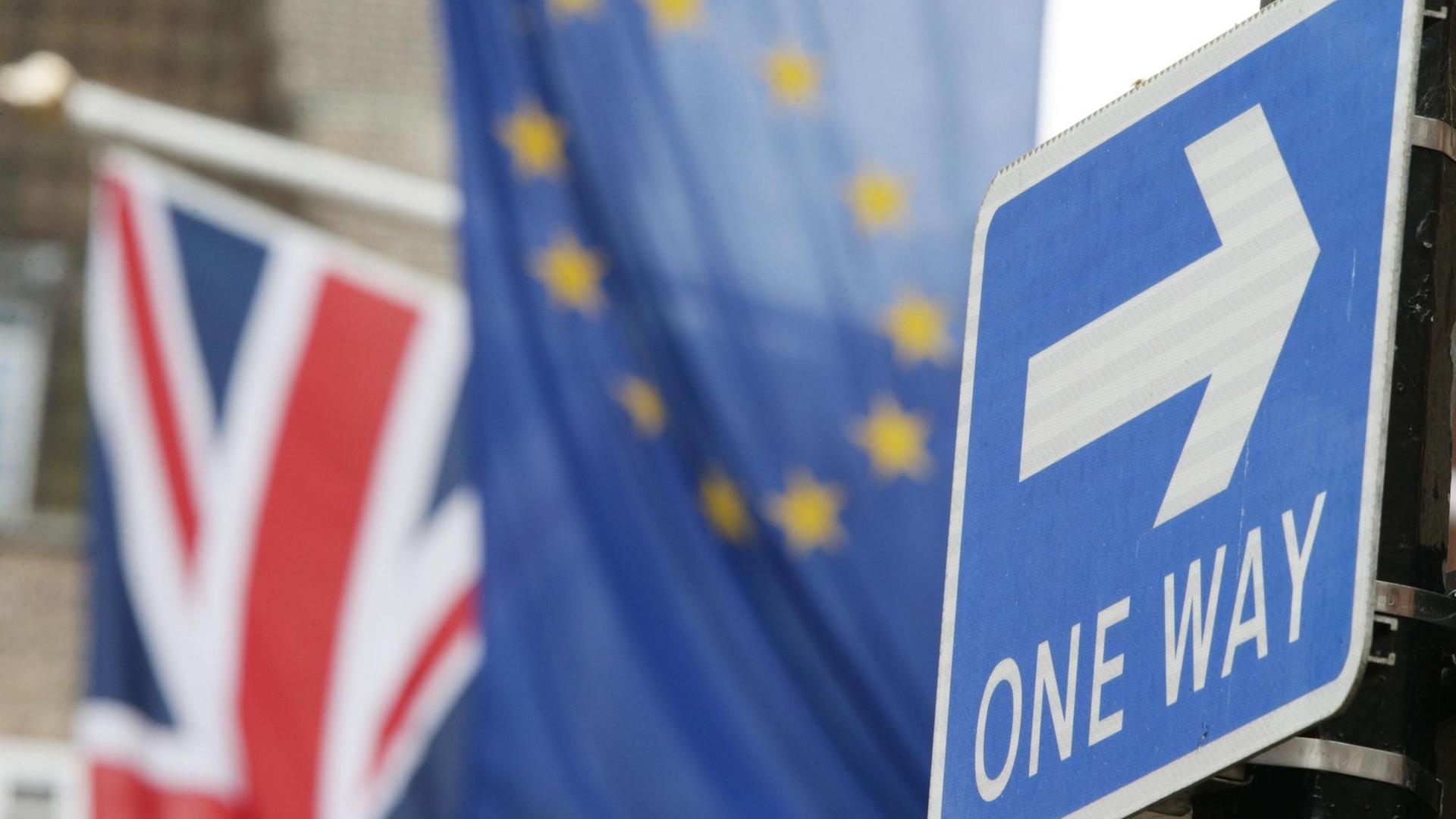 Ein englisches Einbahnstraße-Schild, im Hintergrund sind die Europaflagge und ein Union-Jack zu sehen.