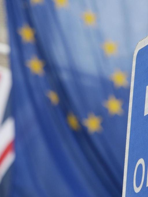 Ein englisches Einbahnstraße-Schild, im Hintergrund sind die Europaflagge und ein Union-Jack zu sehen.
