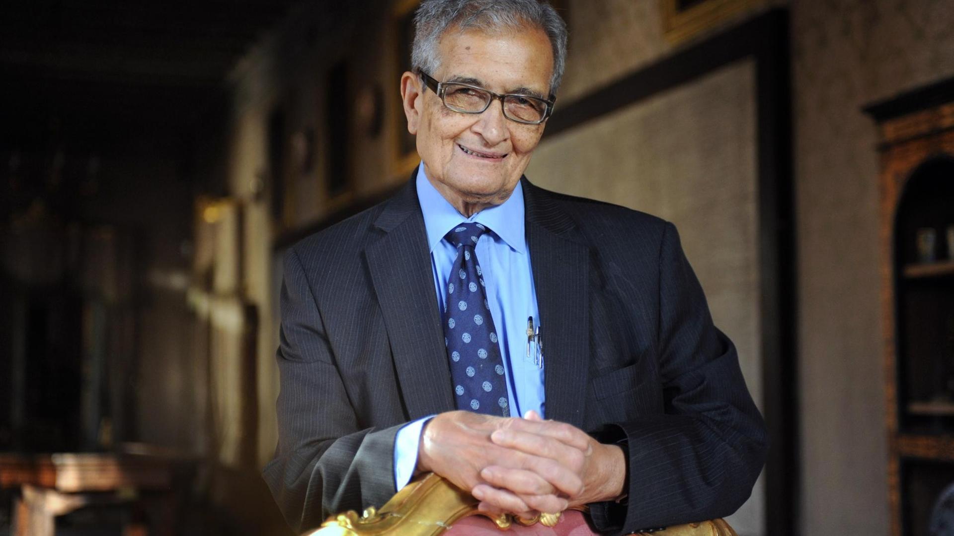 Amartya Sen schaut lächelnd auf einen Stuhl gelehnt in die Kamera.