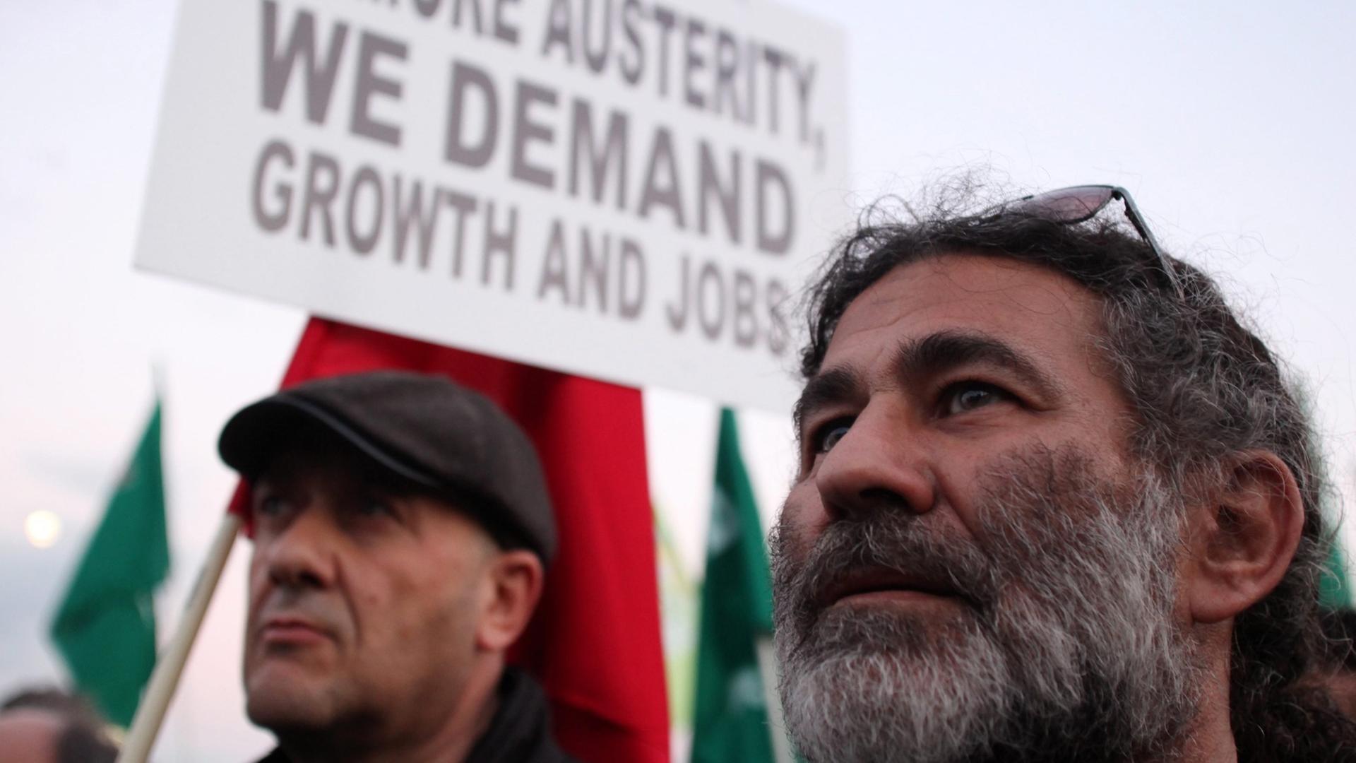 Zwei Demonstranten, im Hintergrund ein Plakat mit der Aufschrift: "No more austerity, we demand jobs and growth" Zwei Demonstranten, im Hintergrund ein Plakat mit der Aufschrift: "No more austerity, we demand jobs and growth"
