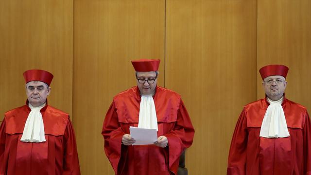 Die drei Richter stehen nebeneinander; Voßkuhle verliest gerade das Urteil, das er in den Händen hält.