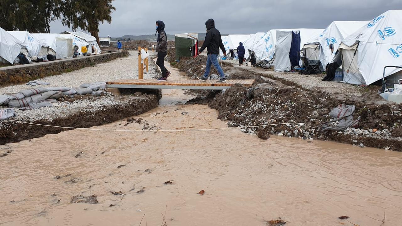 Zwei junge Männer laufen über eine provisorische Holzbrücke zwischen den Zelten unter der ein ganzer Fluß braunes dreckiges Wasser fließt. Mitten durch das Lager. Zwei junge Männer laufen über eine provisorische Holzbrücke zwischen den Zelten unter der ein ganzer Fluß braunes dreckiges Wasser fließt. Mitten durch das Lager.