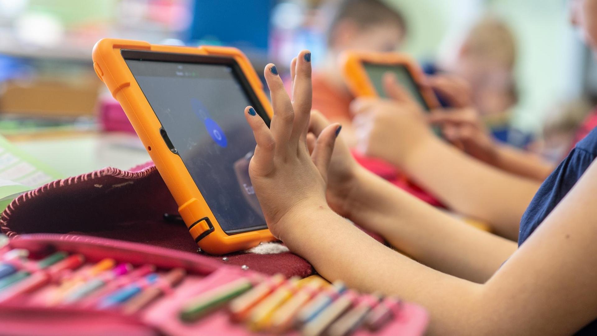 Die Hände eines Mädchens tippen auf einem Tablet, neben ihr liegt ein Mäppchen mit Stiften Die Hände eines Mädchens tippen auf einem Tablet, neben ihr liegt ein Mäppchen mit Stiften
