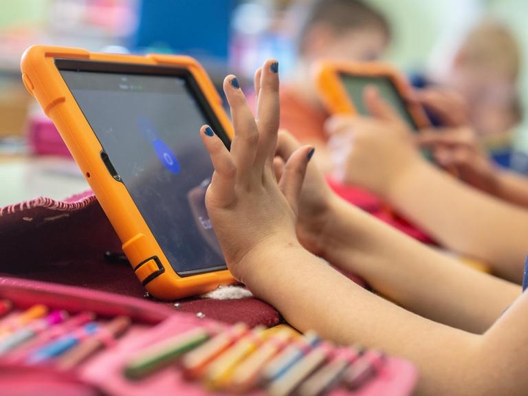 Die Hände eines Mädchens tippen auf einem Tablet, neben ihr liegt ein Mäppchen mit Stiften