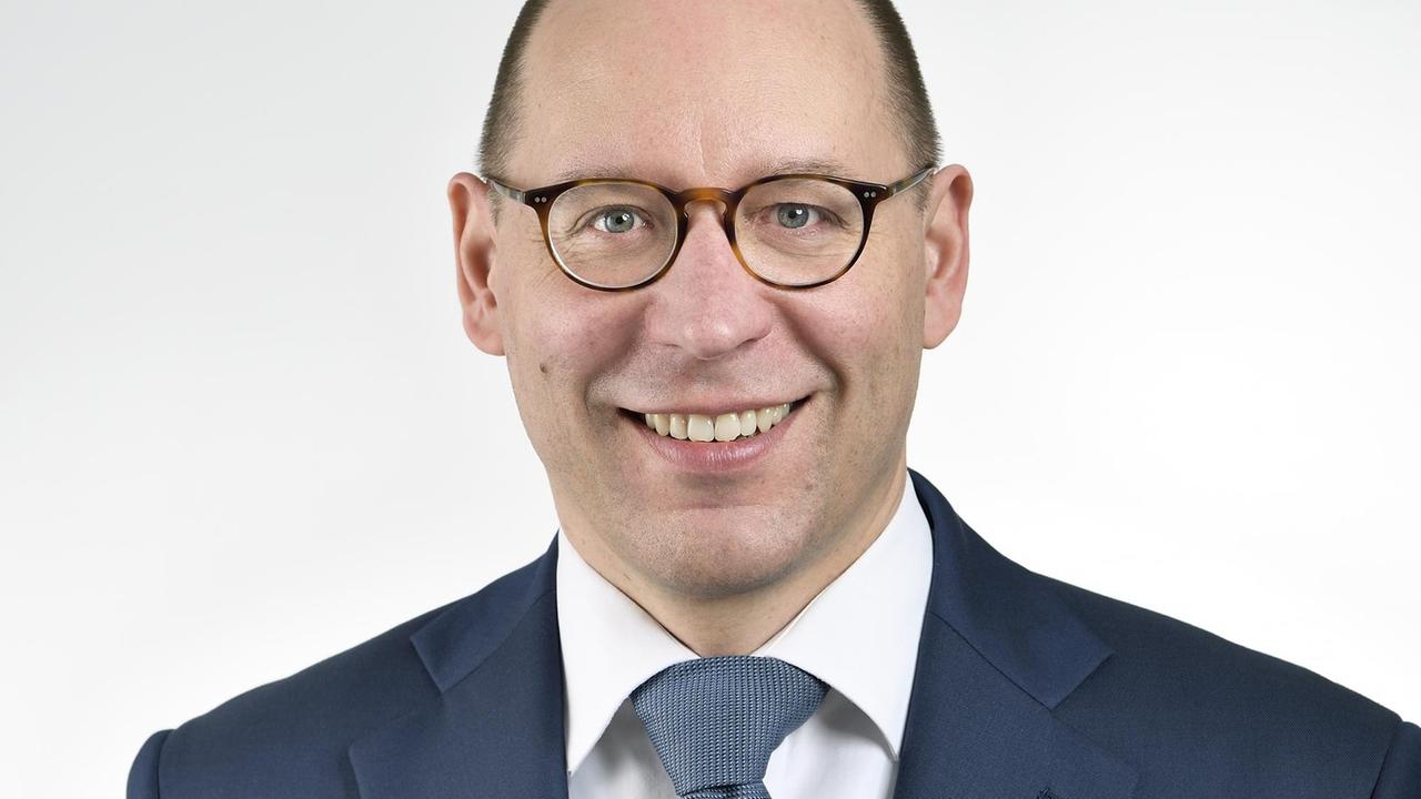 Ein bebrillter Mann im blauen Anzug lächelt in die Kamera. Ein bebrillter Mann im blauen Anzug lächelt in die Kamera.