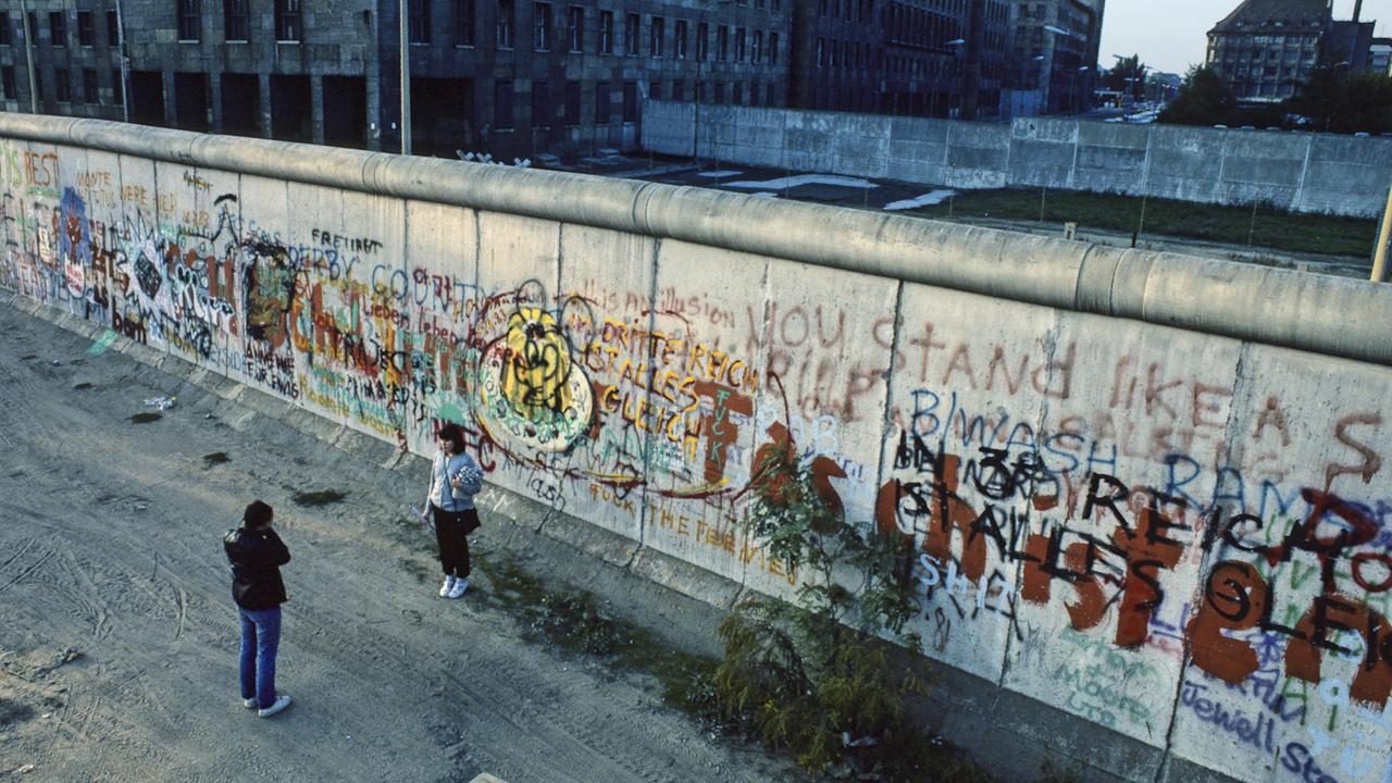 Ein Mann fotografiert eine Frau an der Berliner Mauer vor 1989 an der Wilhelmstrasse.