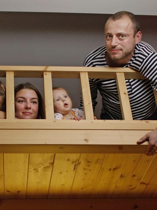 Ein Paar mit zwei Kinder posiert auf einem großen Hochbett für ein Foto.
