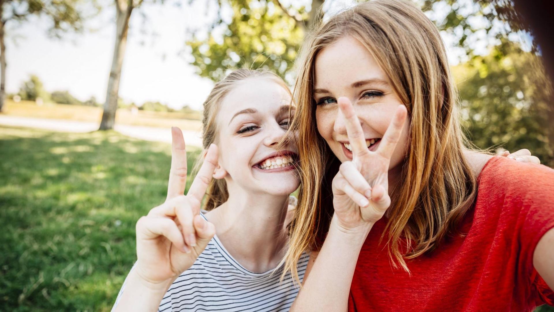 Ein Selfie von zwei Teenagerinnen, die grinsend das Victory-Zeichen machen Ein Selfie von zwei Teenagerinnen, die grinsend das Victory-Zeichen machen