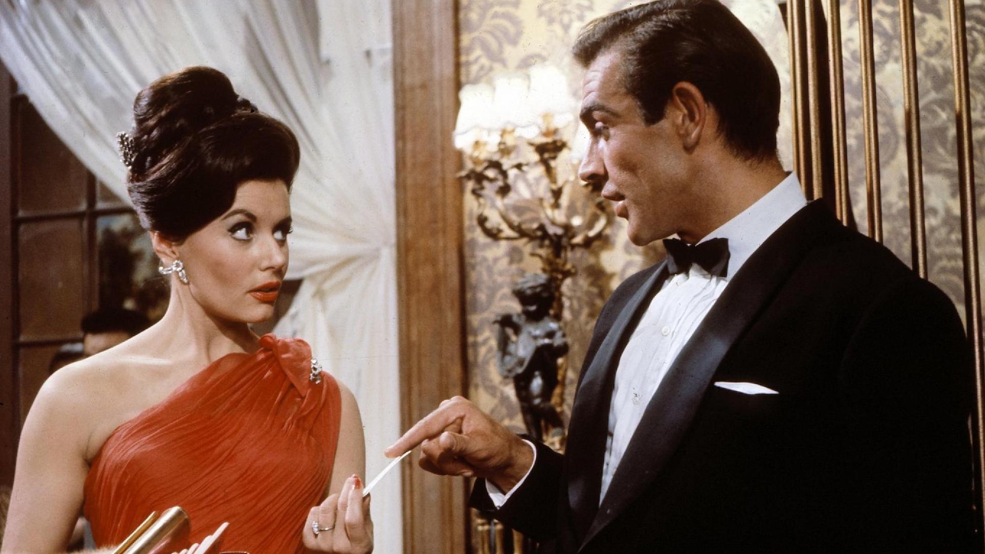 Sean Connery als 007 überreicht Eunice Gaysson als Sylvia in dem britischen Film "James Bond - 007 jagt Dr. No" Casino-Chips. Sean Connery als 007 überreicht Eunice Gaysson als Sylvia in dem britischen Film "James Bond - 007 jagt Dr. No" Casino-Chips.