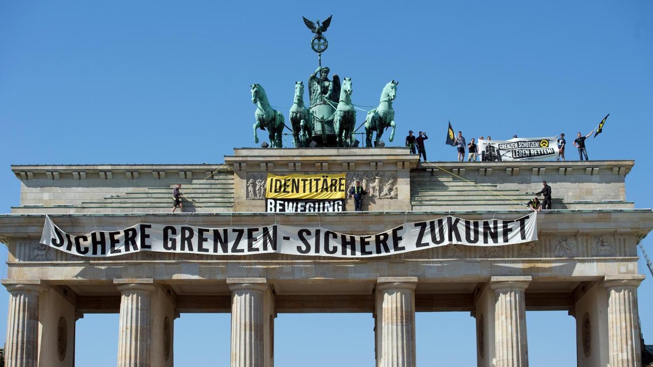 Aktivisten der "Identitären Bewegung" stehen auf dem Brandenburger Tor und entrollen ein Transparent