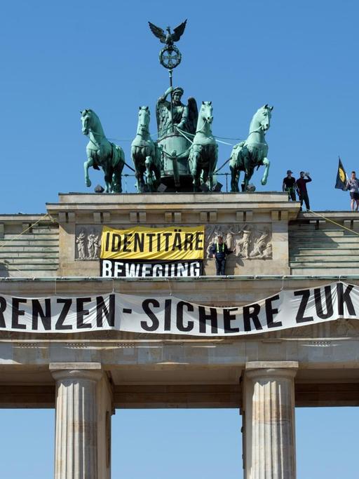 Aktivisten der "Identitären Bewegung" stehen auf dem Brandenburger Tor und entrollen ein Transparent