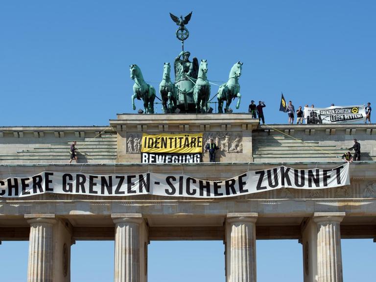 Aktivisten der "Identitären Bewegung" stehen auf dem Brandenburger Tor und entrollen ein Transparent