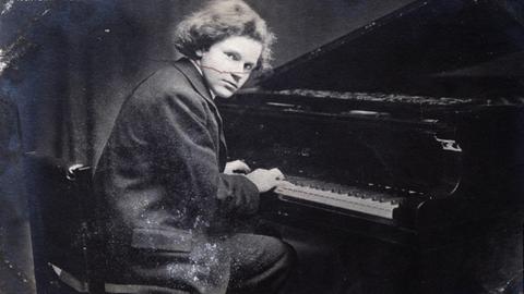 Der junge Pianist Wilhelm Backhaus sitzt am Klavier und spielt. Er schaut in die Kamera. Schwarz-Weiß Fotografie