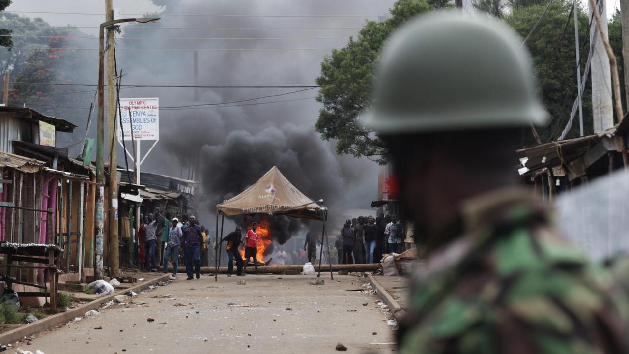 Ein Polizist blickt auf brennende Barikaden und Demonstranten in Kibera, Nairobi Ein Polizist blickt auf brennende Barikaden und Demonstranten in Kibera, Nairobi