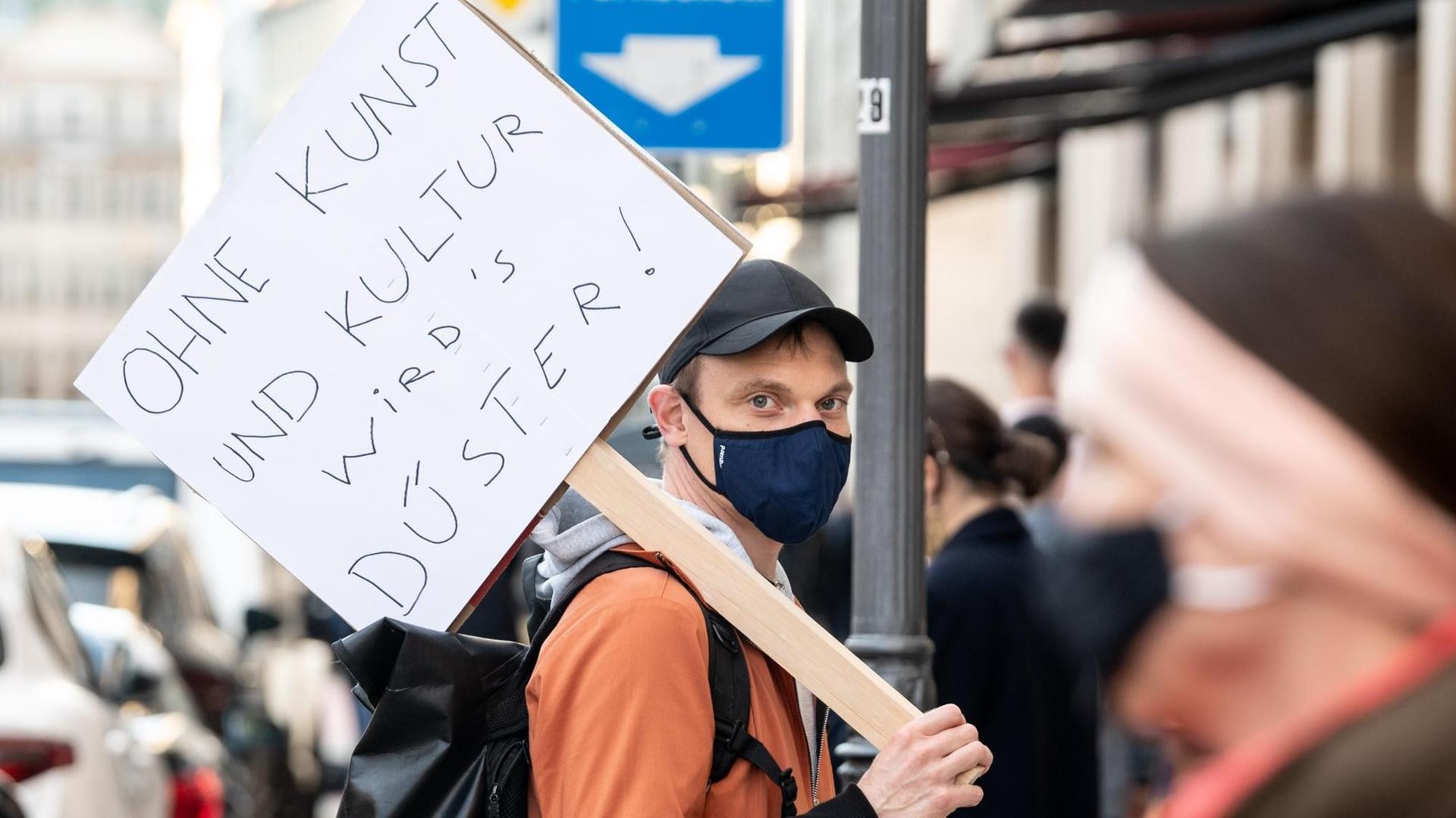 Ein Schauspieler vom Residenztheater steht mit einem Schild mit der Aufschrift „Ohne Kunst und Kultur wirds düster!“ in einer Menschenkette. Ein Schauspieler vom Residenztheater steht mit einem Schild mit der Aufschrift „Ohne Kunst und Kultur wirds düster!“ in einer Menschenkette.