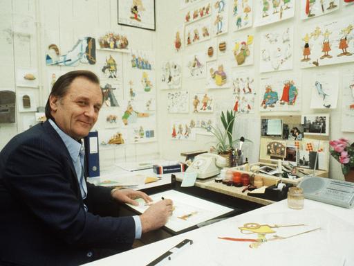 Albert Uderzo sitzt an seinem Schreibtisch und zeichnet, auf dem Tisch einige unfertige Zeichnungen, in den Idefix-Zeichentrick-Studios Paris 1986.