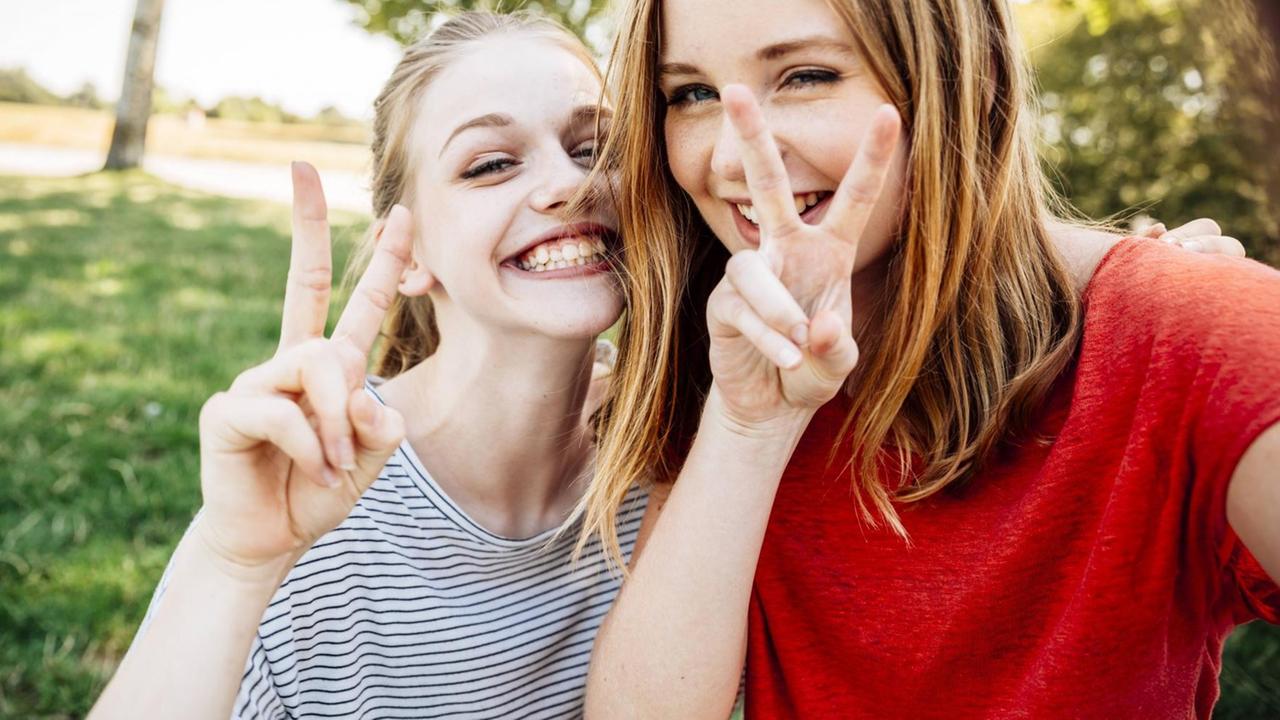 Ein Selfie von zwei Teenagerinnen, die grinsend das Victory-Zeichen machen Ein Selfie von zwei Teenagerinnen, die grinsend das Victory-Zeichen machen