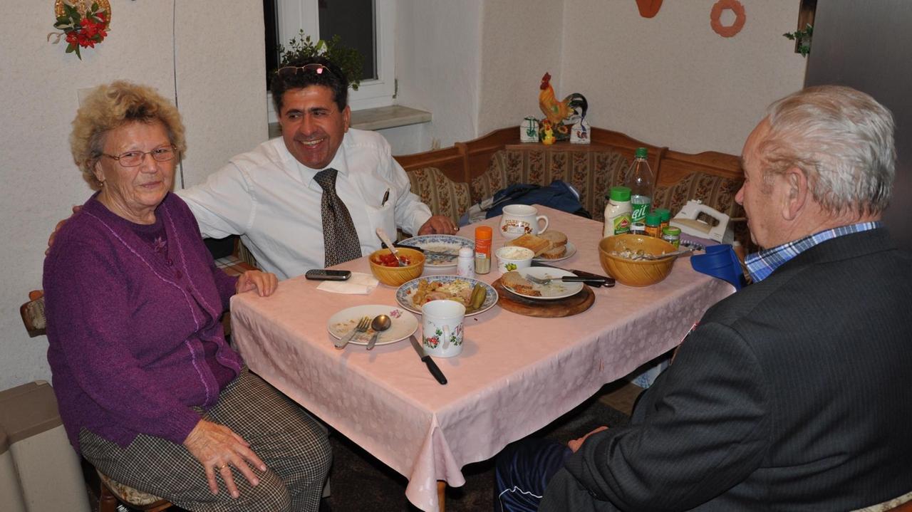 Landarzt Amin Ballouz sitzt mit einem Ehepaar beim Essen.