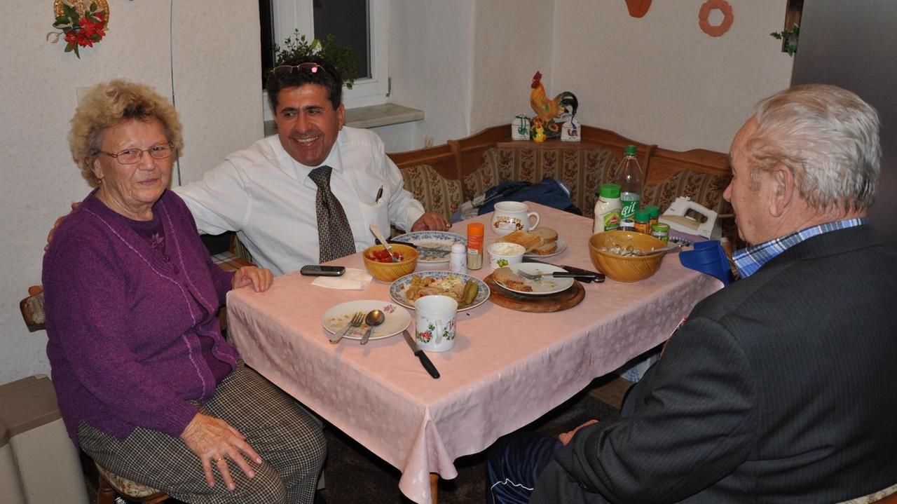 Landarzt Amin Ballouz sitzt mit einem Ehepaar beim Essen. Landarzt Amin Ballouz sitzt mit einem Ehepaar beim Essen.