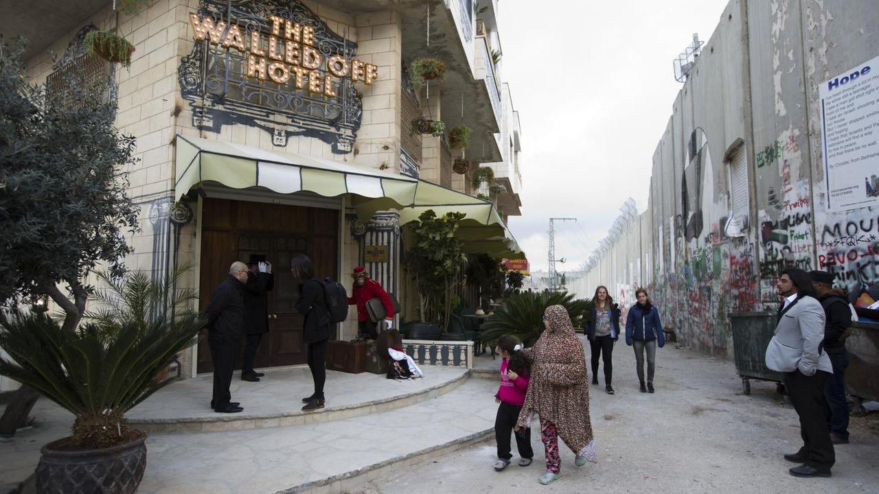 Passanten gehen in Bethlehem (Westjordanland) am Eingangsbereich des "The Walled Off Hotel" und israelischen Sperranlagen vorüber. Das Hotel in der Nähe der israelischen Sperranlagen zeigt Motive des Künstlers Banksy und wirbt mit dem "schlechtesten Blick der Welt". Passanten gehen in Bethlehem (Westjordanland) am Eingangsbereich des "The Walled Off Hotel" und israelischen Sperranlagen vorüber. Das Hotel in der Nähe der israelischen Sperranlagen zeigt Motive des Künstlers Banksy und wirbt mit dem "schlechtesten Blick der Welt".
