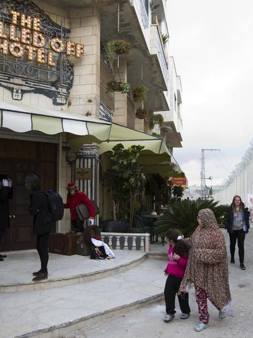 Passanten gehen in Bethlehem (Westjordanland) am Eingangsbereich des "The Walled Off Hotel" und israelischen Sperranlagen vorüber. Das Hotel in der Nähe der israelischen Sperranlagen zeigt Motive des Künstlers Banksy und wirbt mit dem "schlechtesten Blick der Welt".