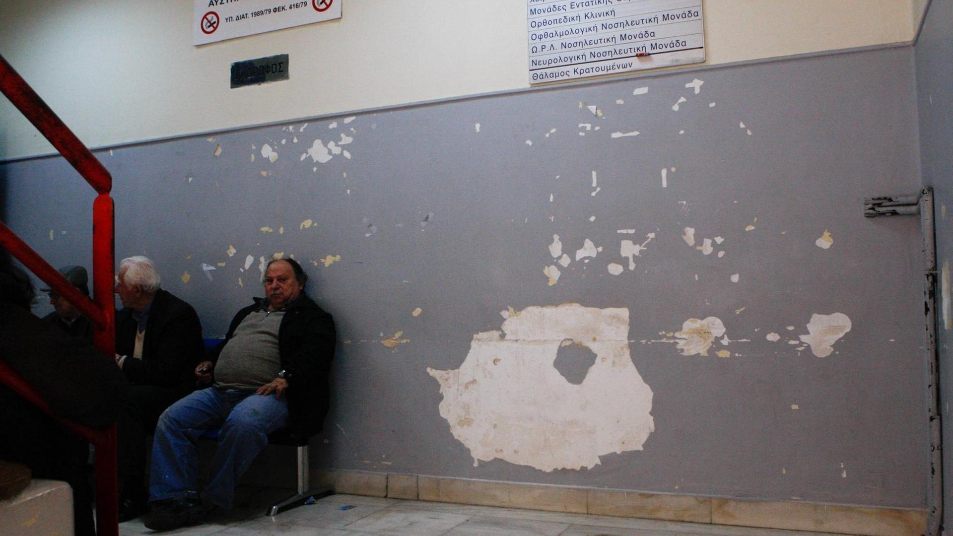Männer sitzen auf Stühlen vor einer Wand mit abgeplatzter Farbe und Putz in einem Krankenhaus und warten.