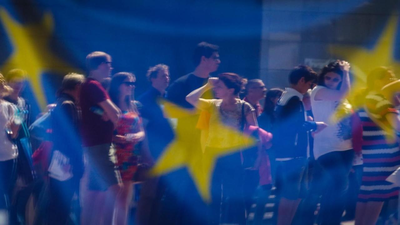 Menschen spiegeln sich in einem Fenster, das mit einer Europa-Flagge behangen ist. Menschen spiegeln sich in einem Fenster, das mit einer Europa-Flagge behangen ist.