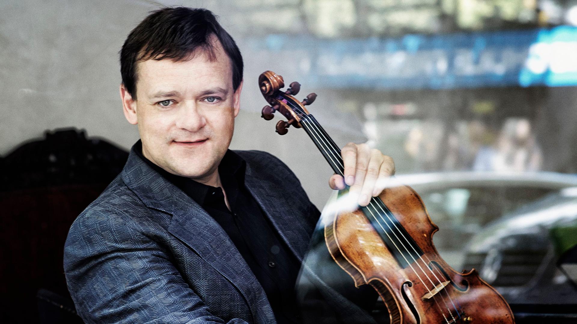 Frank Peter Zimmermann mit seiner Stradivari-Geige, der "Lady Inchiquin". Er sitzt auf einem schwarzen Sessel, trägt ein schwarzes Hemd und ein mittelblaues Jacket und schaut in die Kamera.
die Geige hält er mit der linken Hand vor sich Frank Peter Zimmermann mit seiner Stradivari-Geige, der "Lady Inchiquin". Er sitzt auf einem schwarzen Sessel, trägt ein schwarzes Hemd und ein mittelblaues Jacket und schaut in die Kamera.
die Geige hält er mit der linken Hand vor sich