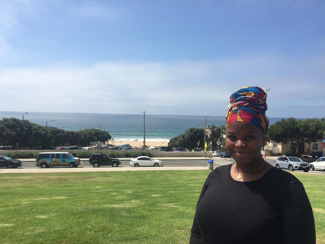 Eine junge Frau mit buntem Turban steht auf einer grünen Wiese vor einem Strandpanorama. Eine junge Frau mit buntem Turban steht auf einer grünen Wiese vor einem Strandpanorama.