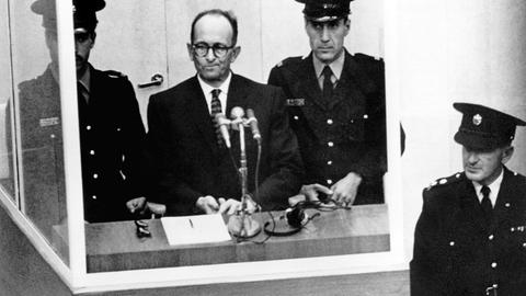 Der NS-Kriegsverbrecher Adolf Eichmann während seiner Vernehmung am ersten Prozesstag vor dem Jerusalemer Bezirksgericht am 11.4.1961. Vor ihm steht ein Mikrofon, neben ihm zwei Wachen.
