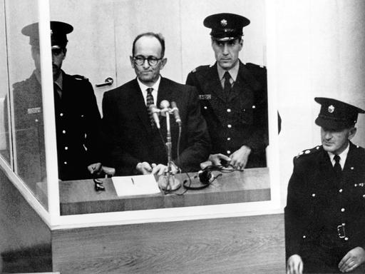 Der NS-Kriegsverbrecher Adolf Eichmann während seiner Vernehmung am ersten Prozesstag vor dem Jerusalemer Bezirksgericht am 11.4.1961. Vor ihm steht ein Mikrofon, neben ihm zwei Wachen.