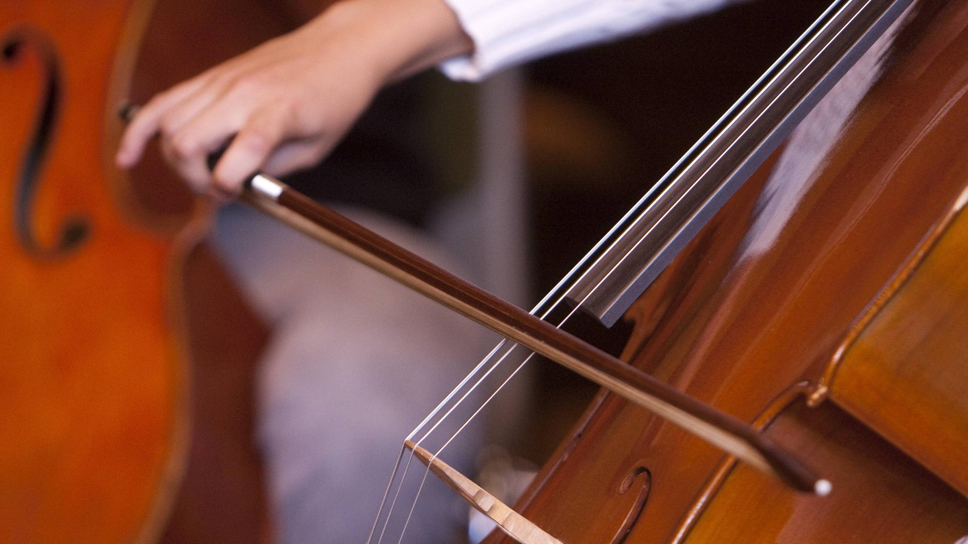 Eine jugendliche Hand führt einen Bogen beim Cello-Spiel.