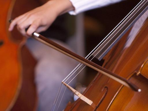 Eine jugendliche Hand führt einen Bogen beim Cello-Spiel.