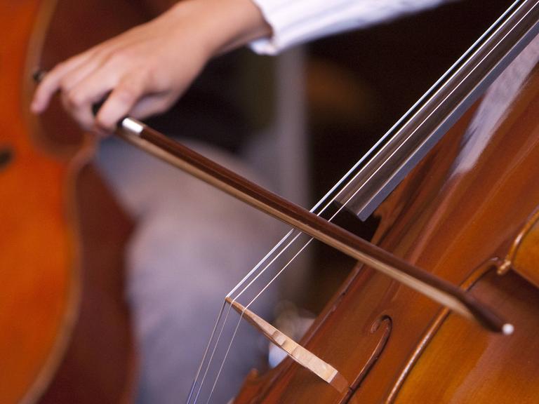 Eine jugendliche Hand führt einen Bogen beim Cello-Spiel.