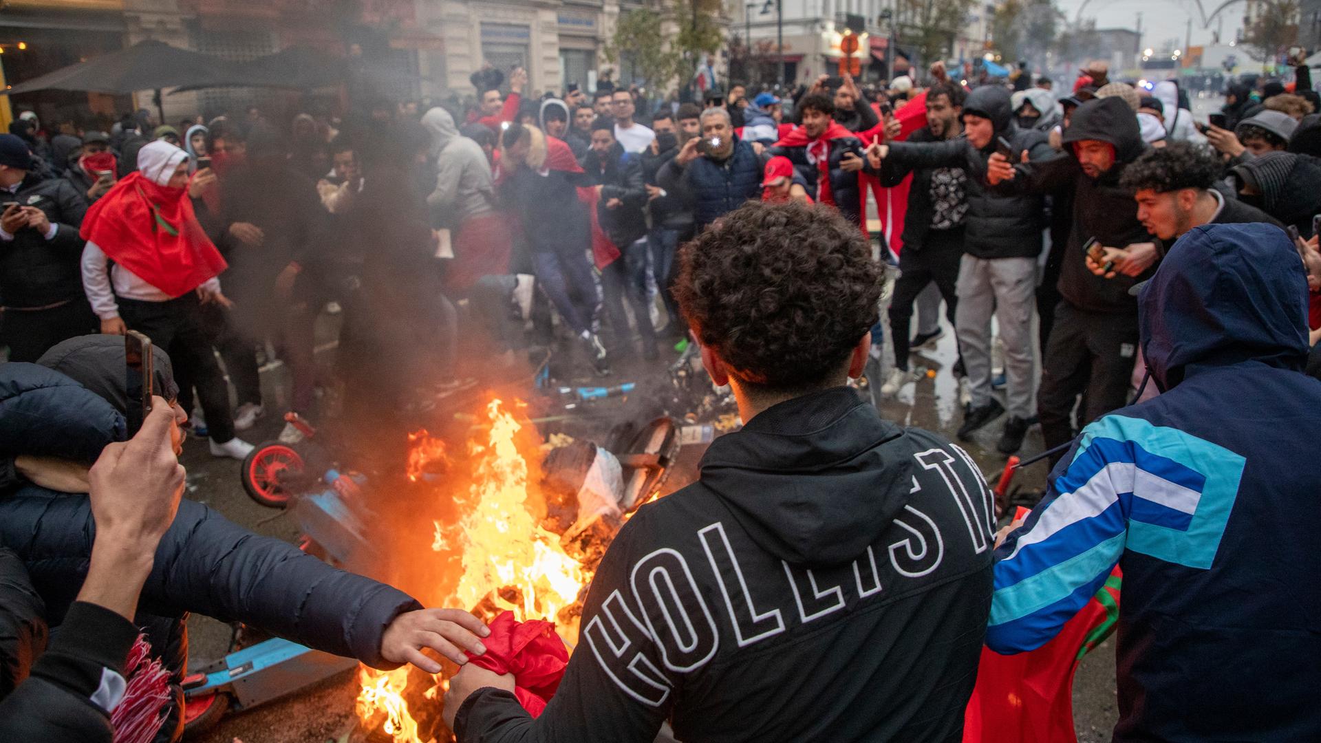 Jugendliche randalieren in der Stadt Brüssel. Sie stehen im Kreis um brennende Gegenstände, darunter ein E-Roller. 