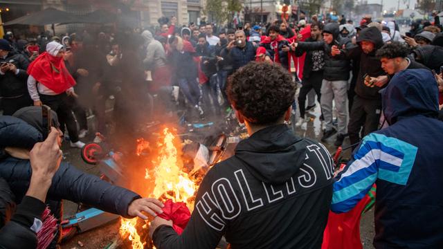 Jugendliche randalieren in der Stadt Brüssel. Sie stehen im Kreis um brennende Gegenstände, darunter ein E-Roller. 