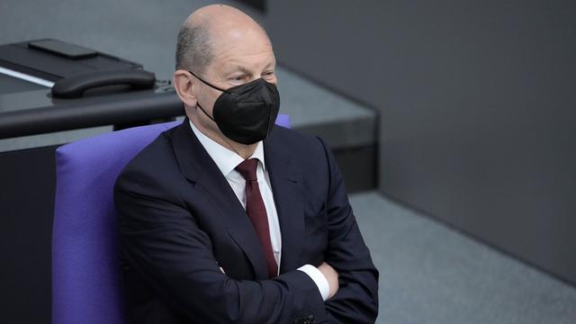 Bundeskanzler Olaf Scholz im Porträt. Er sitzt im Bundestag und trägt einen schwarzen Mund-Nasen-Schutz.