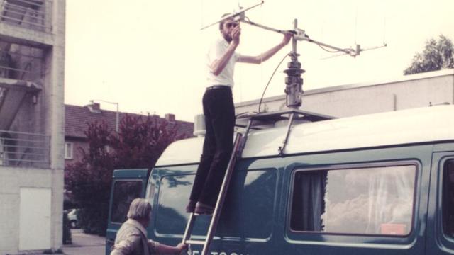 Zwei Techniker stehen an einem Ü-Wagen des Deutschlandfunk und richten die Antenne, 1984
