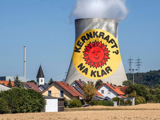 Eine Fotomontage zeigt den Slogan "Kernkraft na klar" auf dem Kühlturm des Atomkrafwerks Isar 2, der weit über den Wohnhäusern der nahelegenen Ortschaft rausragt.