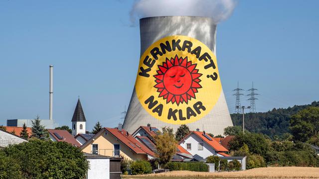Eine Fotomontage zeigt den Slogan "Kernkraft na klar" auf dem Kühlturm des Atomkrafwerks Isar 2, der weit über den Wohnhäusern der nahelegenen Ortschaft rausragt.