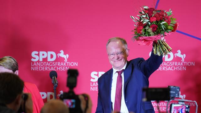 Stephan Weil (SPD), der Ministerpräsident von Niedersachsen, hält einen Blumenstrauß in der Hand und steht auf einer Bühne, deren rote Rückwand mit SPD beschriftet ist