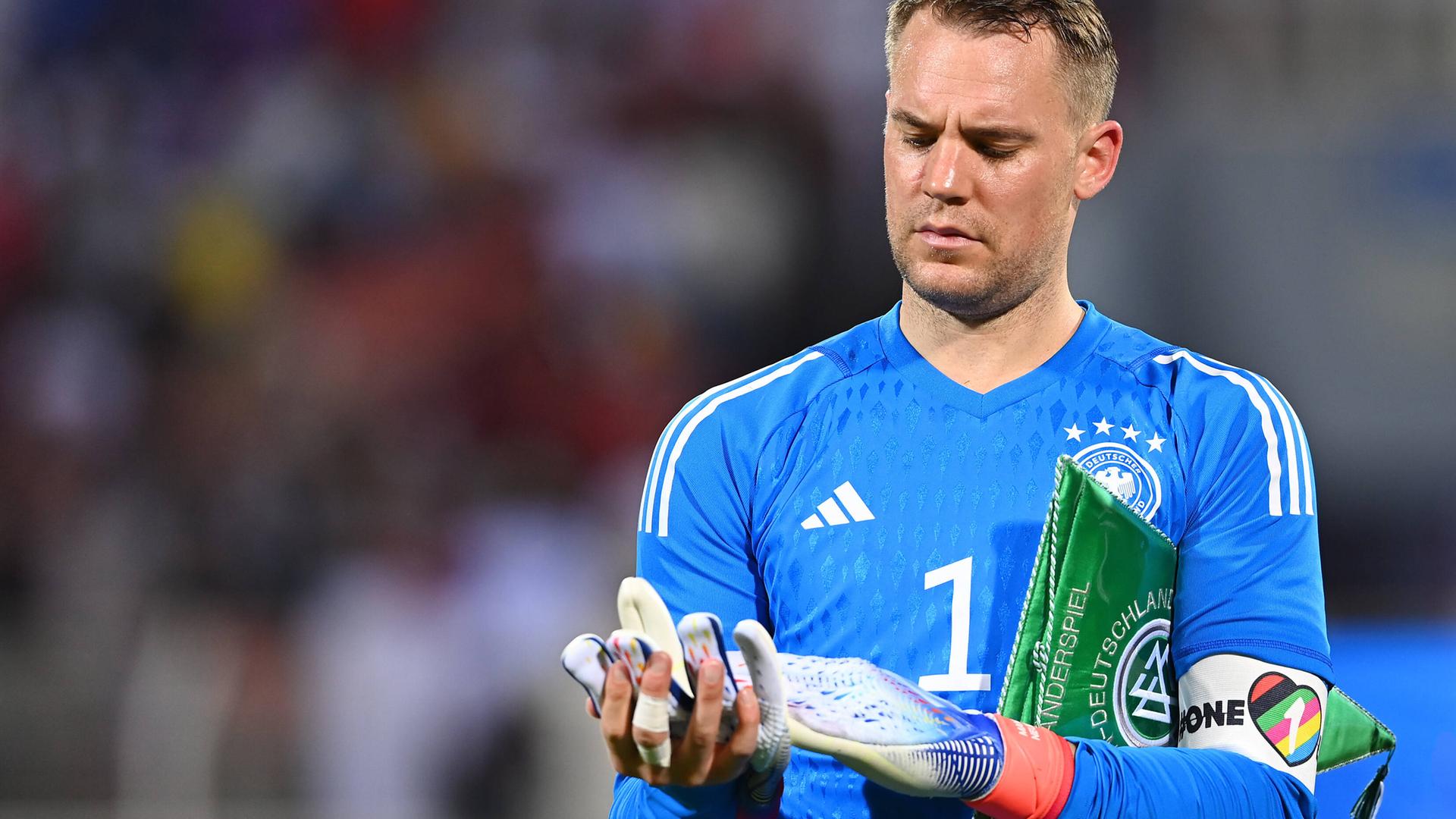 Der Torwart Manuel Neuer zieht sich einen Spielerhandschuh aus, am Arm trägt er eine Armbinde mit der Aufschrift "One Love" und einem Herz in Regenbogenfarben. Der Torwart Manuel Neuer zieht sich einen Spielerhandschuh aus, am Arm trägt er eine Armbinde mit der Aufschrift "One Love" und einem Herz in Regenbogenfarben.