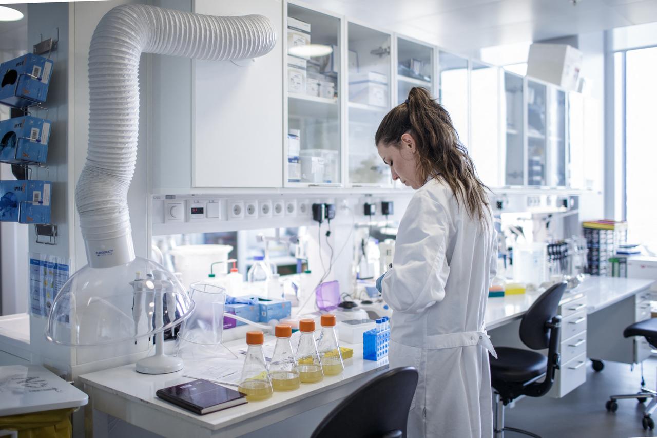 Eine Frau im weißen Kittel steht in einem Labor, in dem Impfstoffe entwickelt werden.