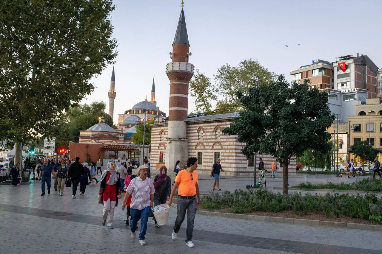 Menschen laufen mit vollen Körben und Tüten aus einem Markt über einen weitläufigen Platz. Menschen laufen mit vollen Körben und Tüten aus einem Markt über einen weitläufigen Platz.